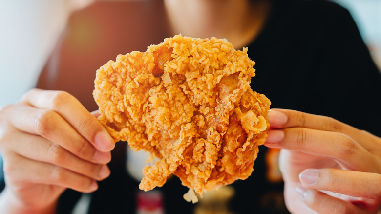 Hands holding a piece of fried chicken