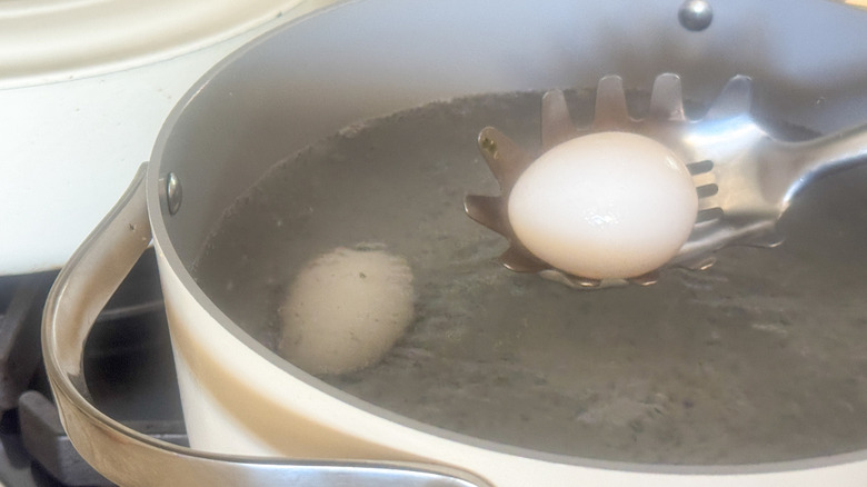 slotted spoon placing egg into boiling water