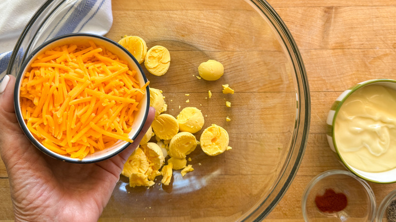 hand holding bowl of shredded cheese over bowl of egg yolks