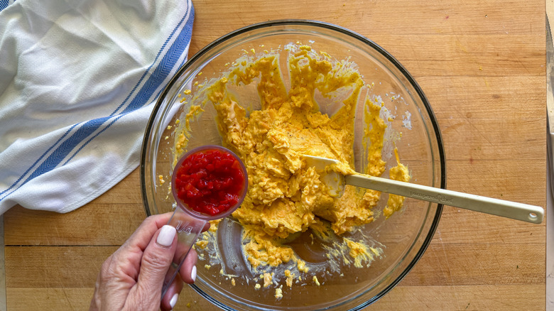 hand adding pimentos to bowl with deviled egg filling