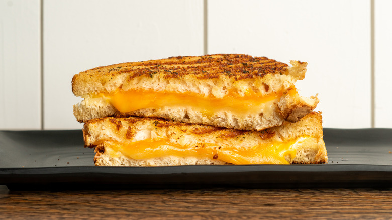 Grilled cheese sandwich cut in half, one piece stacked on top of the other, on a rectangular black plate on a wooden table