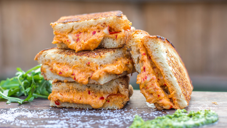 Pimento grilled cheese sandwich quarters stacked on a wooden table surrounded by salt sprinkles and herbs