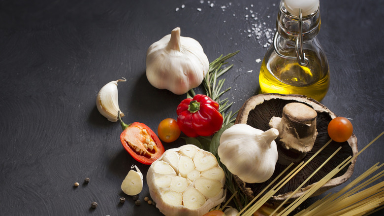 Garlic, peppers, mushroom, rosemary, peppercorns, flaky salt, dried pasta, and olive oil on a slate table.
