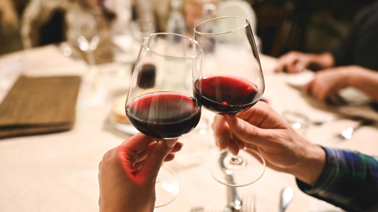 People's hands are seen toasting with red wine at a restaurant table.