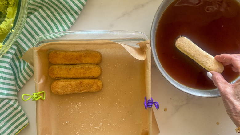 hand dipping ladyfinger into espresso
