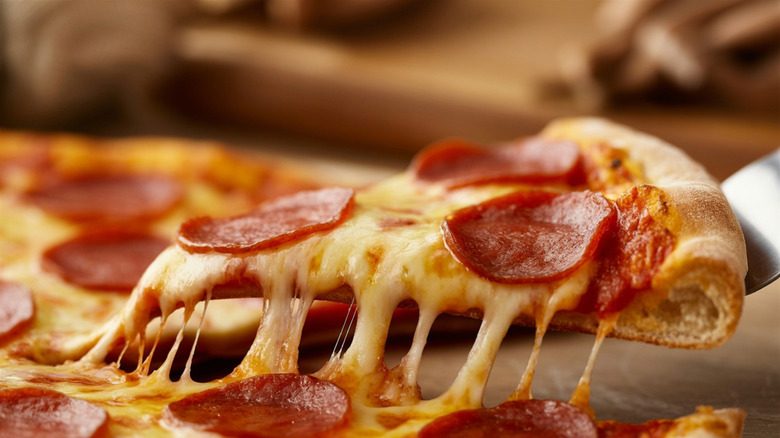 Someone using a spatula to lift a slice of pepperoni pizza