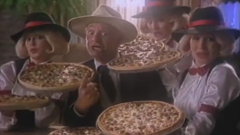 Screenshot of a vintage Godfather's Pizza commercial, with the Godfather and three women in fedoras