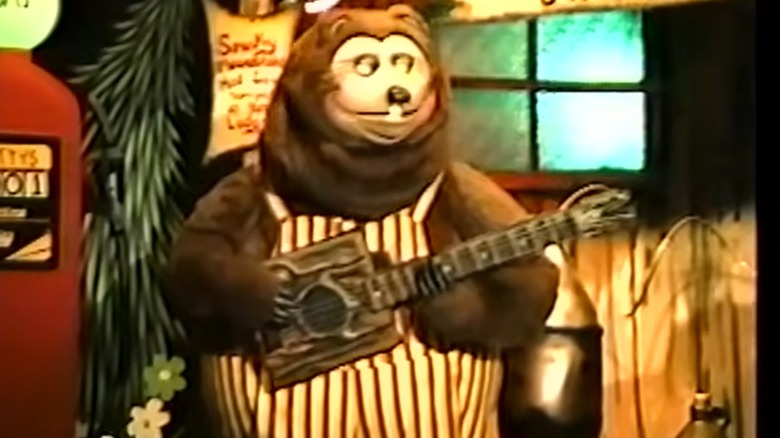Screenshot from a vintage video of Showbiz Pizza's Rock-afire band featuring a bear in striped overalls playing guitar