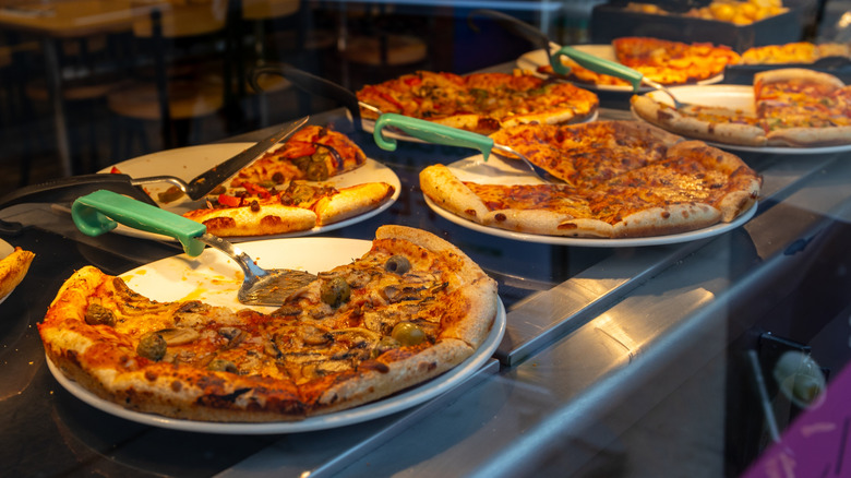 Multiple pizzas lined up on serving trays on a pizza buffet