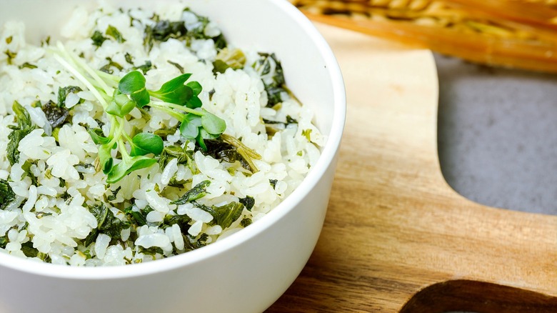 White rice with fresh herbs and chopped cooked greens in a white bowl over a wooden serving board.