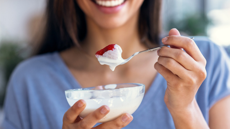 Smiling woman eating a spoonful of yogurt with a strawberry on her spoon