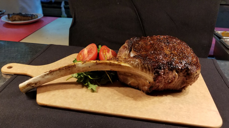 Tomahawk steak from Fleming's Prime Steakhouse and WIne Bar on a plate with tomatoes and lettuce