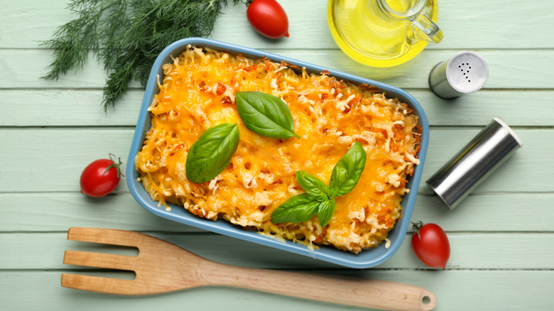 Cheesy baked pasta on green table with ingredients.