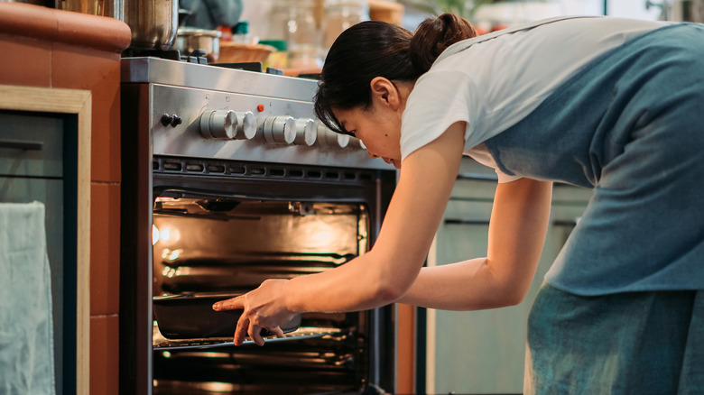 woman sliding covered pan into oven