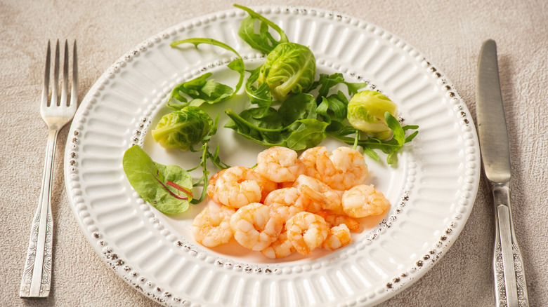 Cooked shrimp on a white place accompanied by fresh greens