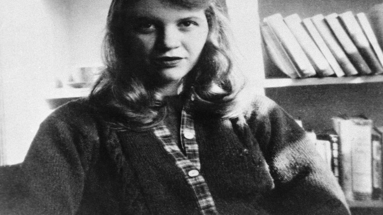 Sylvia Plath in front of a bookshelf in black and white.