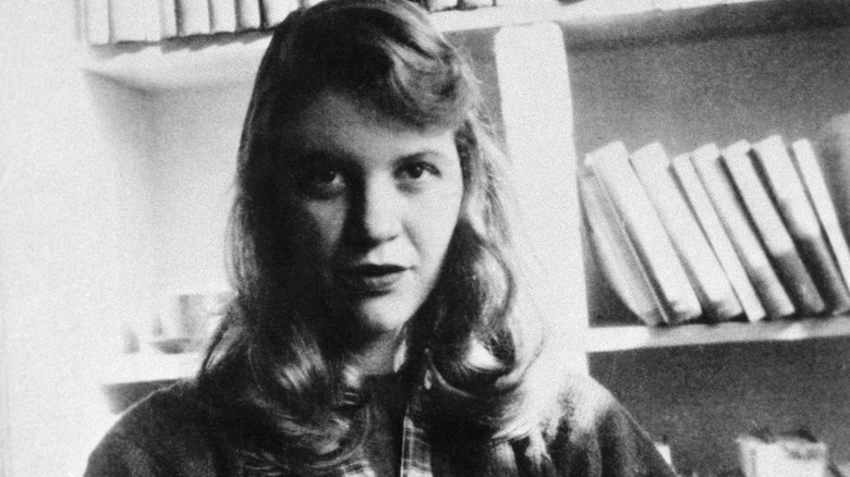 Sylvia Plath in front of a bookshelf in black and white.