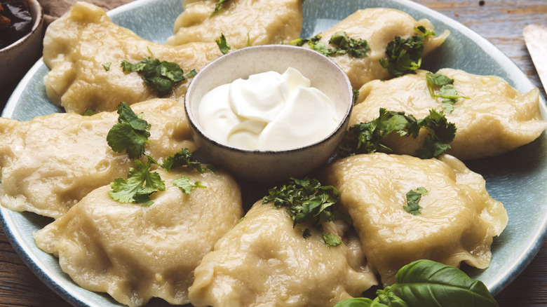 Boiled pierogi placed around a side of sour cream.
