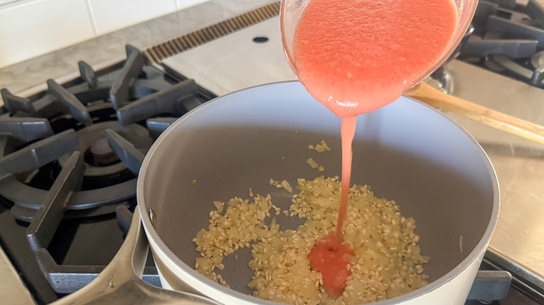 hand pouring tomato puree into pot