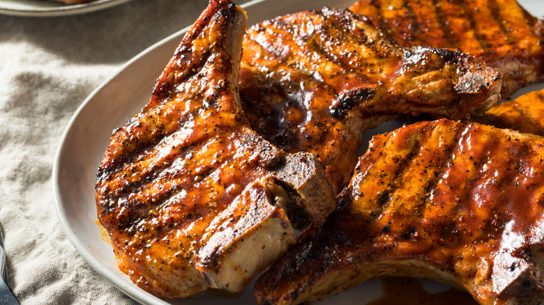 Four pieces of grilled pork chops on the bone covered by a chili sauce in a white plate
