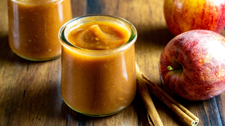 Jar of apple butter with cinnamon and apples on the side