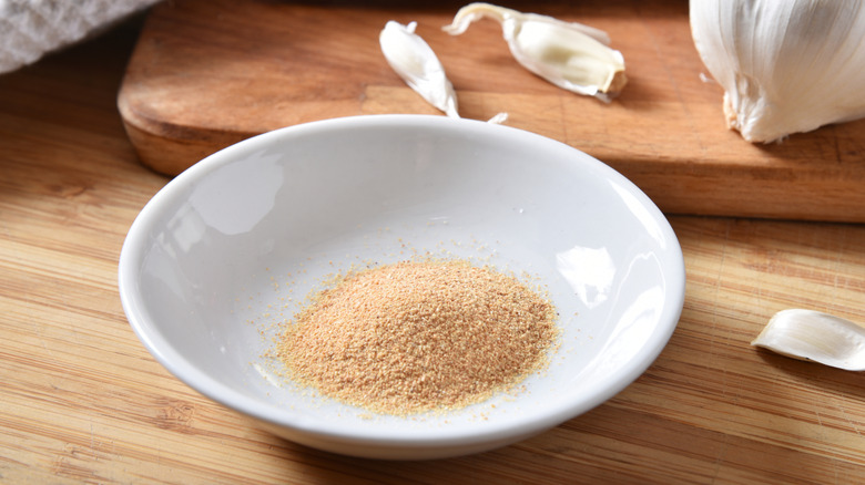 Bowl of garlic powder on a wooden background, garlic cloves around it