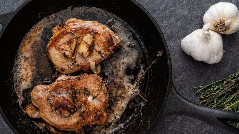 Pork chops in a pan with garlic and herbs on the side