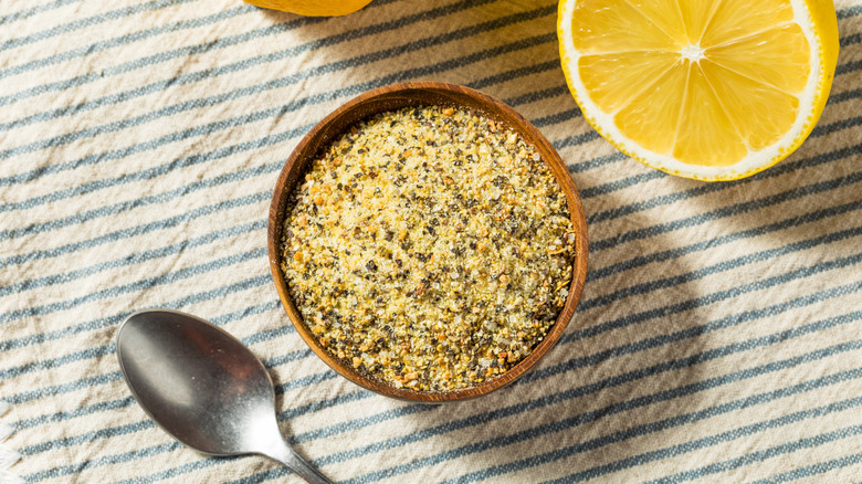 Bowl of lemon pepper seasoning on a cloth with a spoon and lemon half next to it
