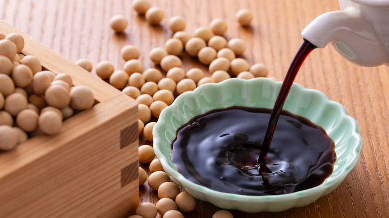 Pot pouring soy sauce into bowl, with soy beans in the background