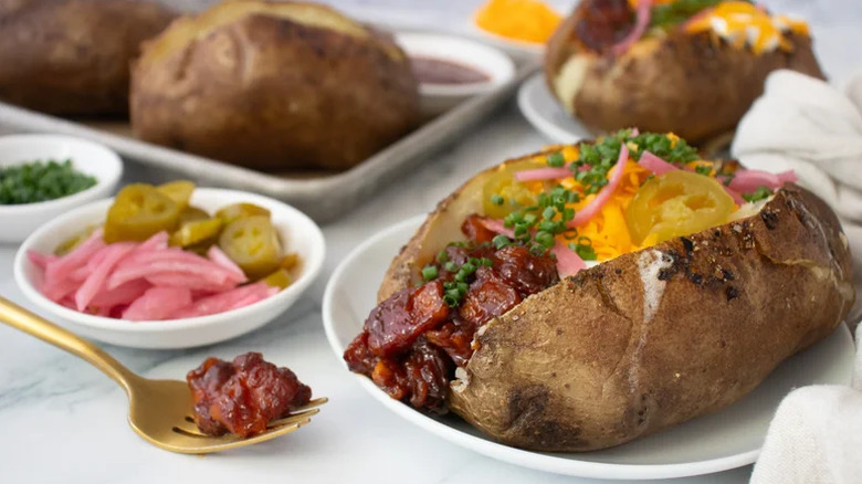 Baked potatoes on plate with various fillings like pork belly, cheese, chives, jalapeños, and pickled red onions.