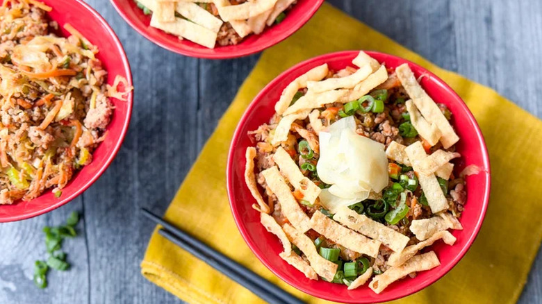Three bowls of pork egg roll mixture topped with scallions, ginger, and strips of crispy fried wontons.