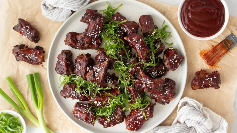 Pork riblets on a white plate topped with sesame seeds and scallions.