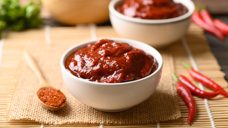 A bowl of gochujang sauce sits on a wooden board.