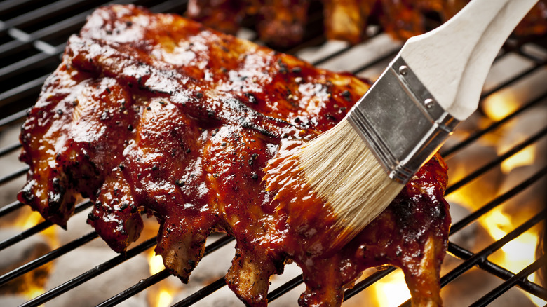 A rack of pork ribs is being glazed on the grill with sauce.