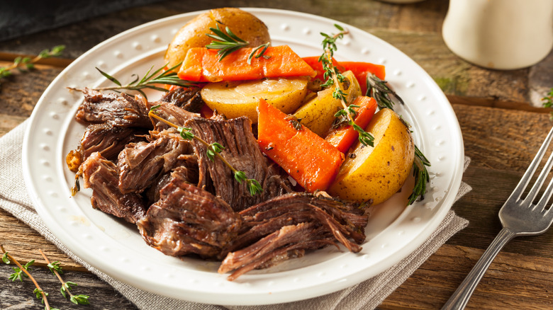 Pot roast with vegetables sits on a plate topped with fresh herbs.