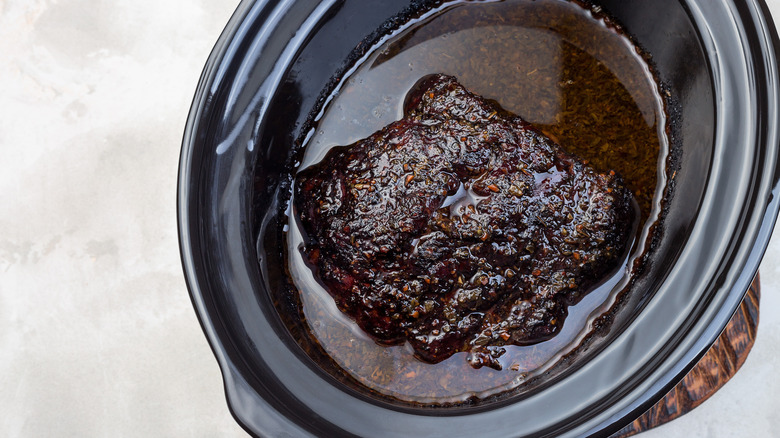 Top down view of a pot roast simmering in a slow cooker