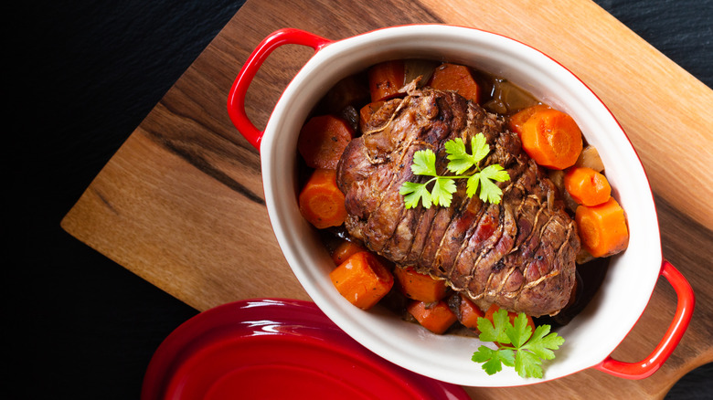 A pot roast sitting in the pot surrounded by sauce and carrots