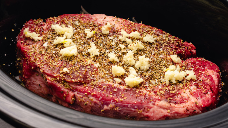 Raw beef chuck roast with seasonings in a slow cooker.