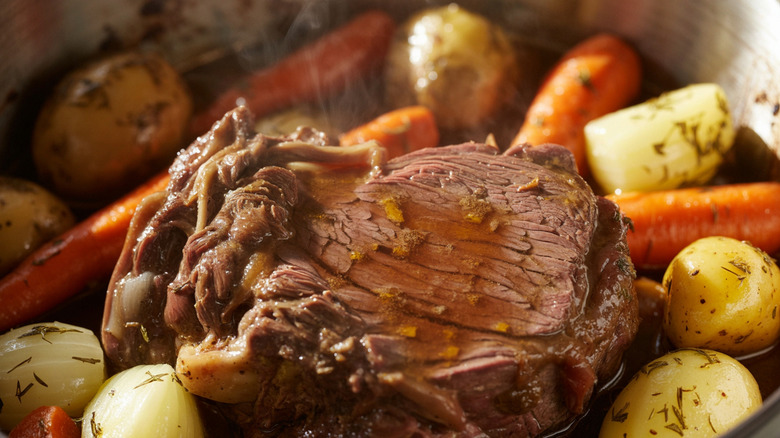 Cooked pot roast in a pot with onions, potatoes, carrots, and herbs
