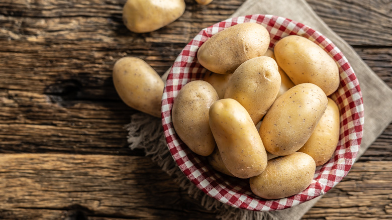 Raw potatoes in a basket on a wooden table