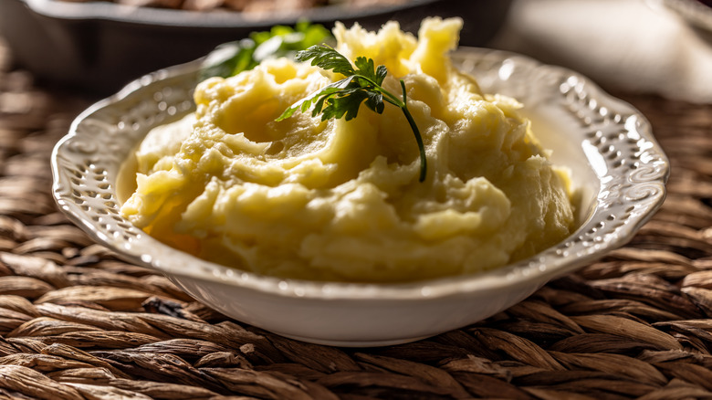 Mashed potatoes topped with parsley in a white bowl on a rustic table