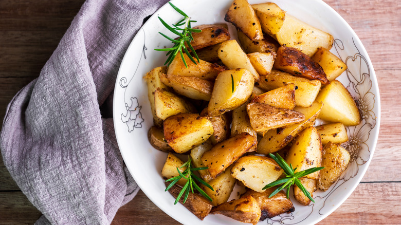 Roast potatoes with rosemary in a white bowl on a wooden table