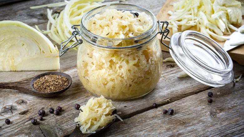 Jar of sauerkraut on a wooden surface with cabbage and spices on the side