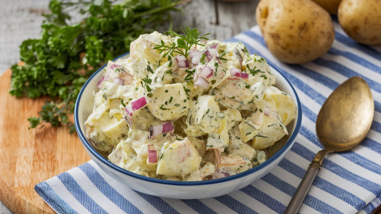 Potato salad in a bowl topped with herbs and diced red onion