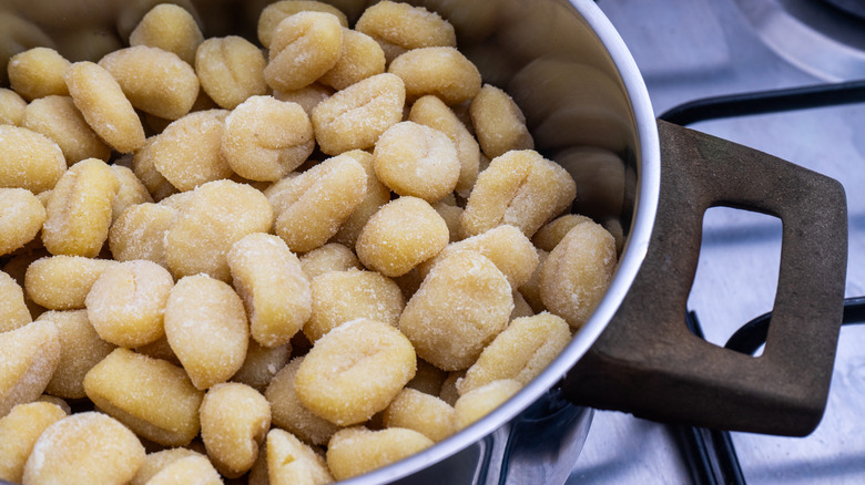 A pan of gnocchi simmering over a flame on a stovetop in a traditional restaurant kitchen