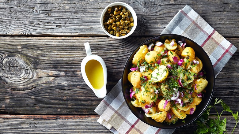 Top-down view of potato salad in a bowl made with baby gold potatoes, chopped red onion, fresh herbs, and capers