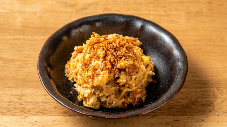 Potato salad topped with crispy fried onions in a brown bowl on a tabletop