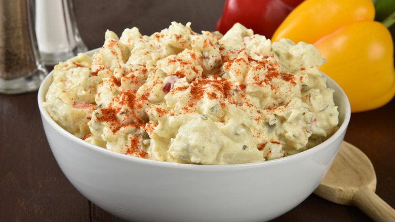 A bowl of potato salad garnished with paprika on a wooden table