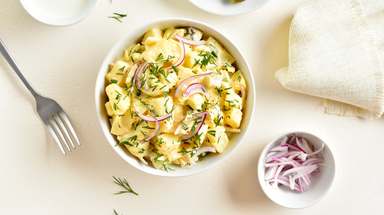 A creamy bowl of potato salad with slices of red onion and touches of garnish