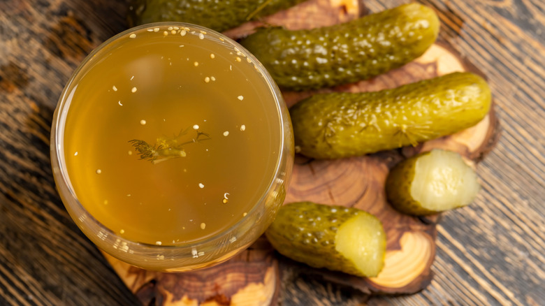 Pickles sitting beside a glass of pickle juice.